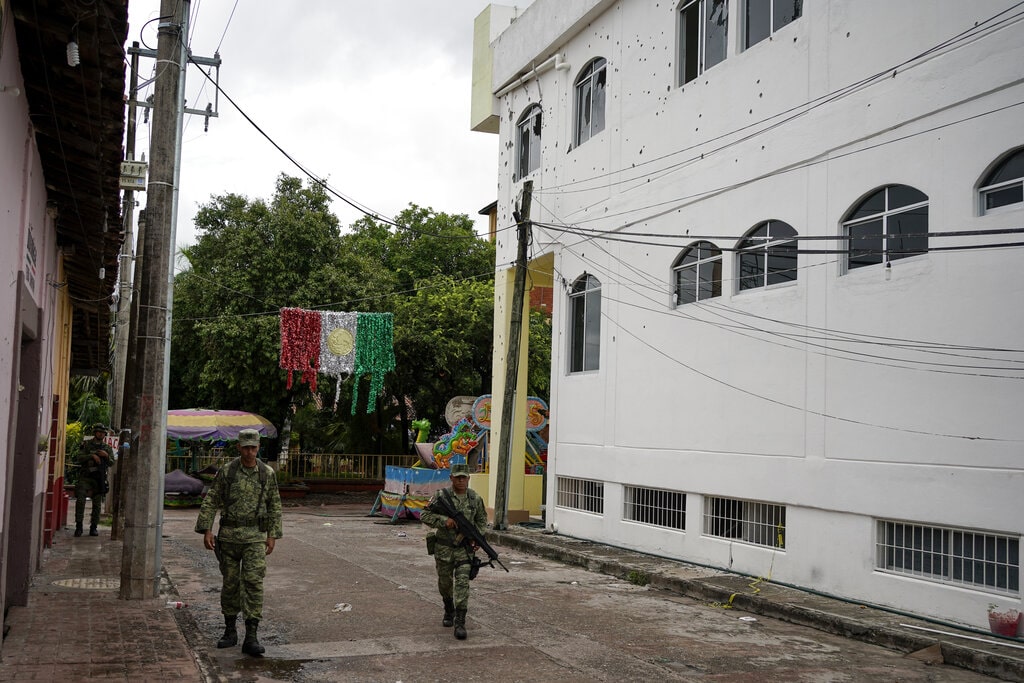 Soldiers walk past the City Hall pocketed with bullet holes the day after a mass shooting in San Miguel Totolapan, Mexico, Thursday, Oct. 6, 2022.